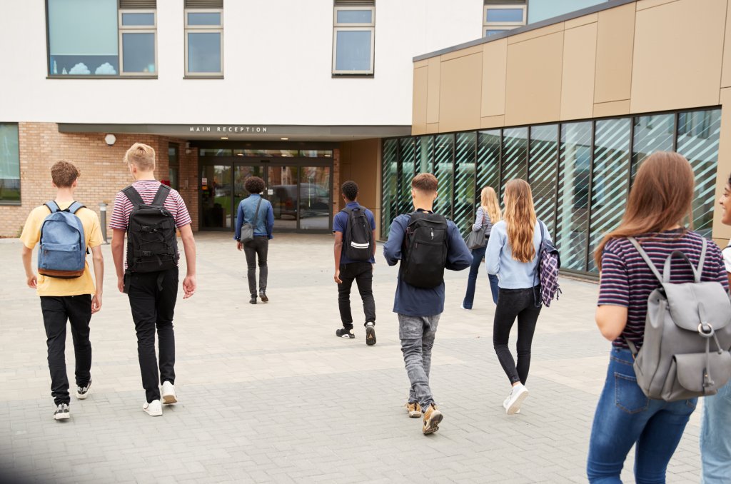 Rear View Of High School Students Walking Into College Building Together