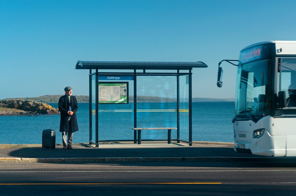En mann står på en bussholdeplass og venter på bussen som kommer